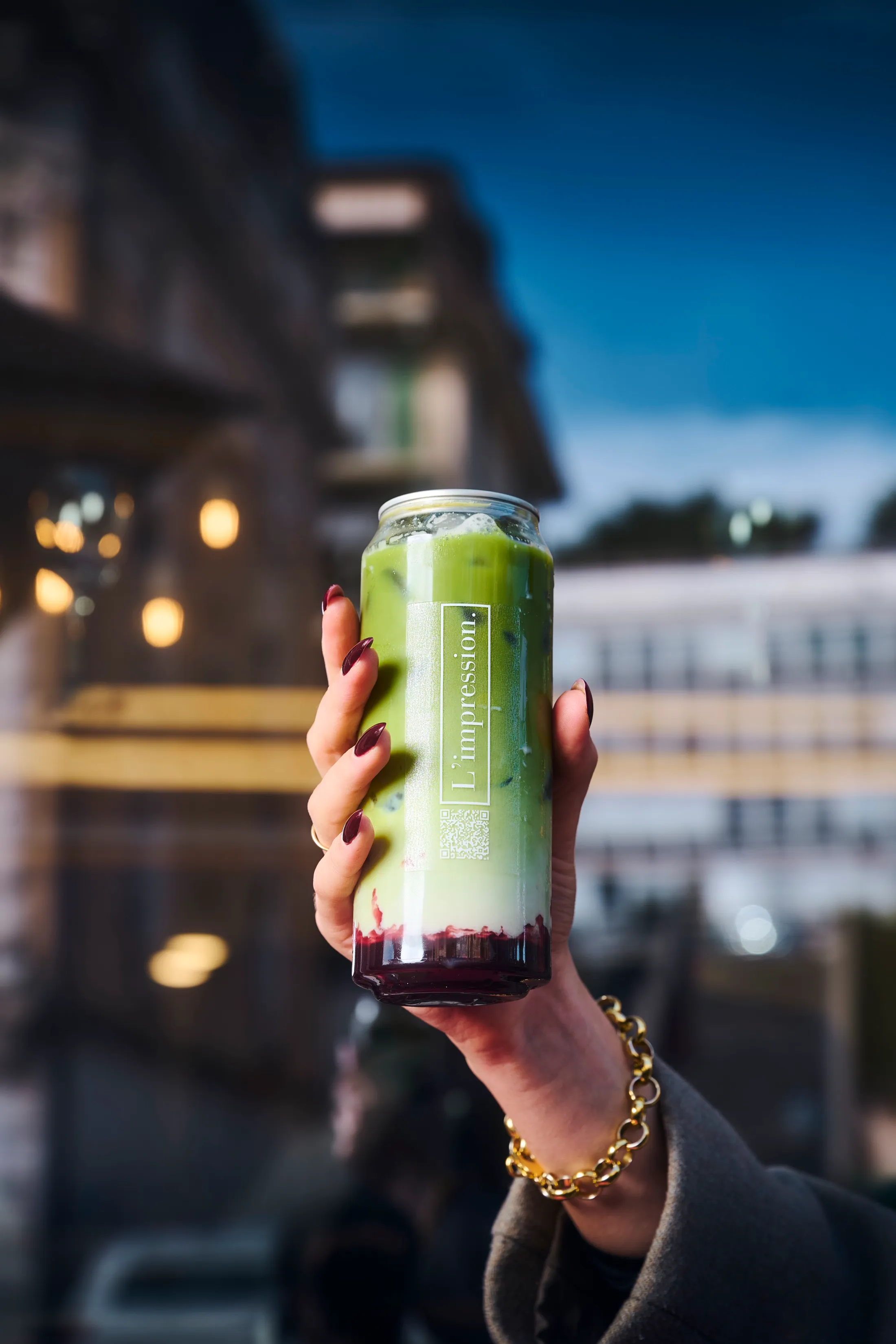 L'Impression iced matcha held up at dusk, Lausanne evening lights in the background