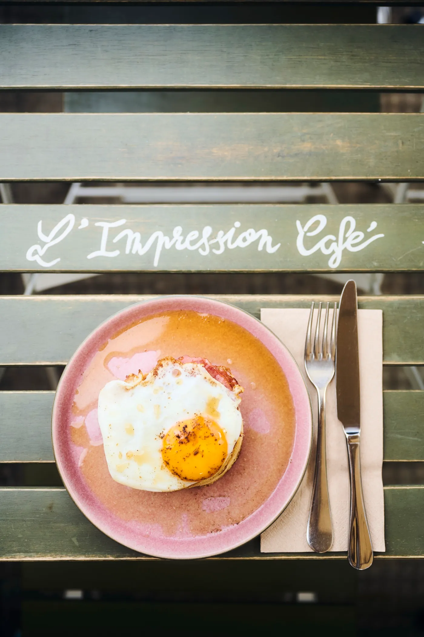 Fried egg and ham served on a terrace bench, hand-painted L’Impression Café lettering